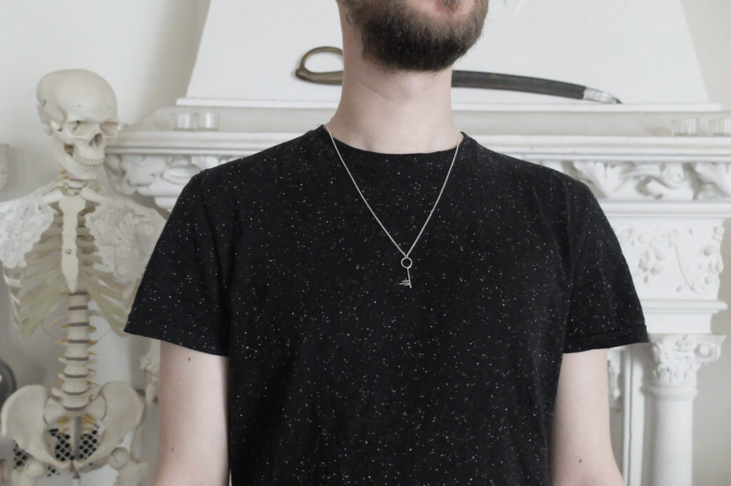 bearded man wearing a back t-shirt with adistressed silver key pendant, skeleton in the background