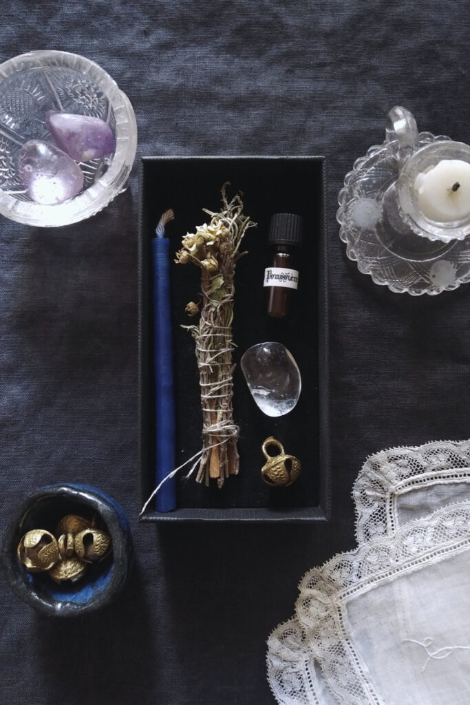 Mini candle, mini vial, bell and crystal quartz, on dark fabric, with antique lace handkerchief