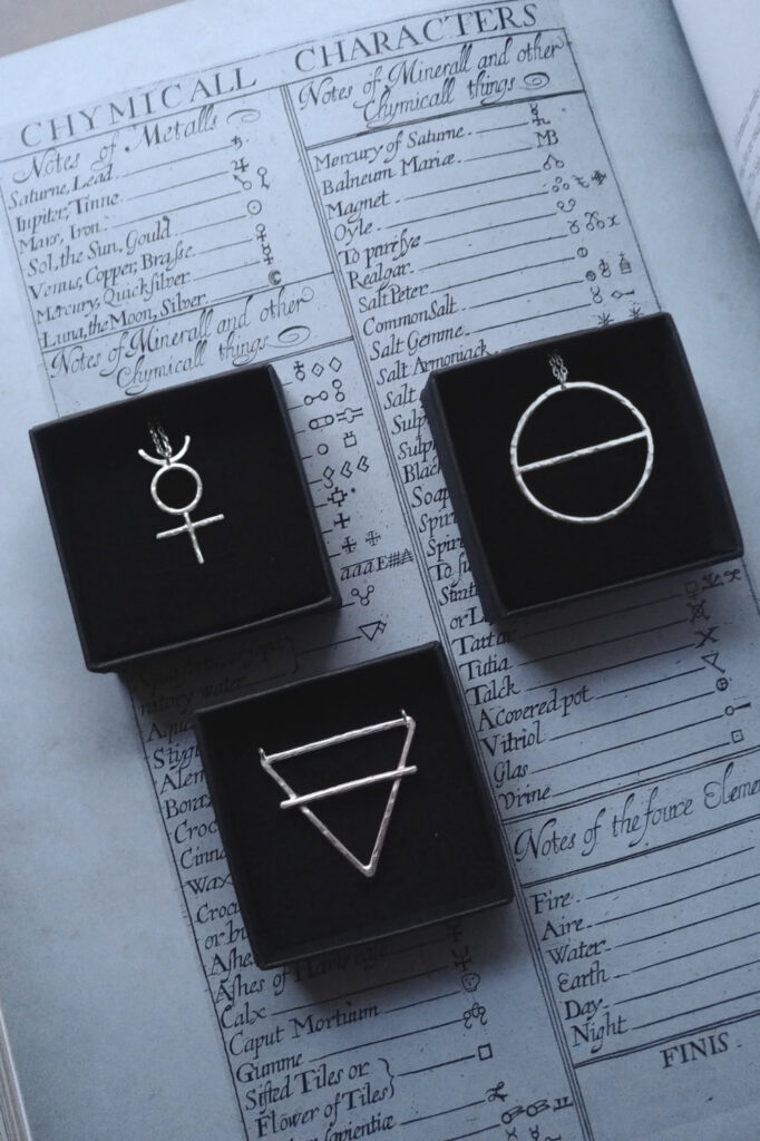 silver pendant of the alchemical symbols Mercury, Salt & Earth on an old chemical table