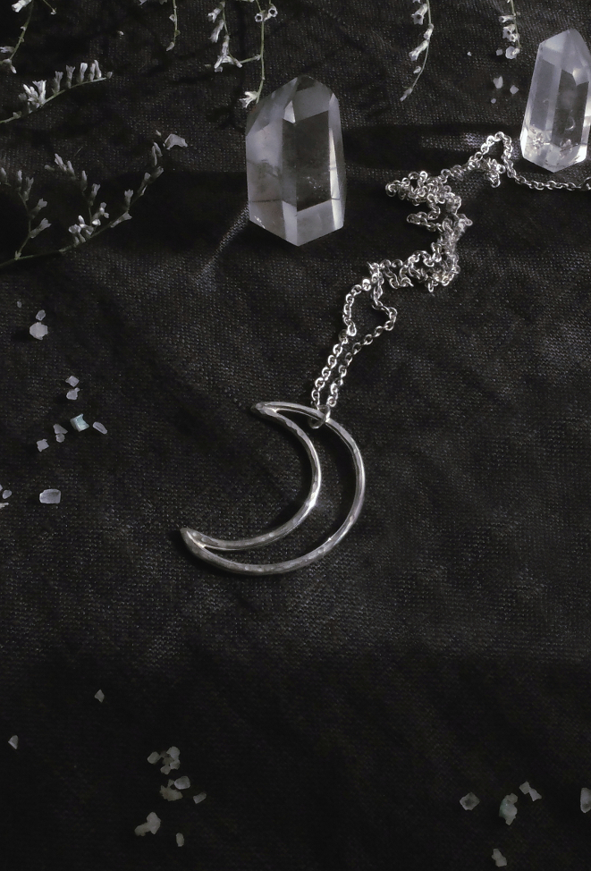 silver pendant of the alchemical symbol Moon on a dark cloth with crystal points