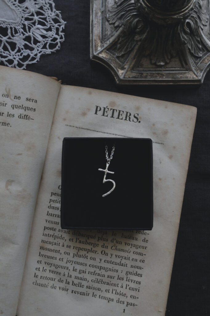 silver pendant of the alchemical symbol Saturn on an old book