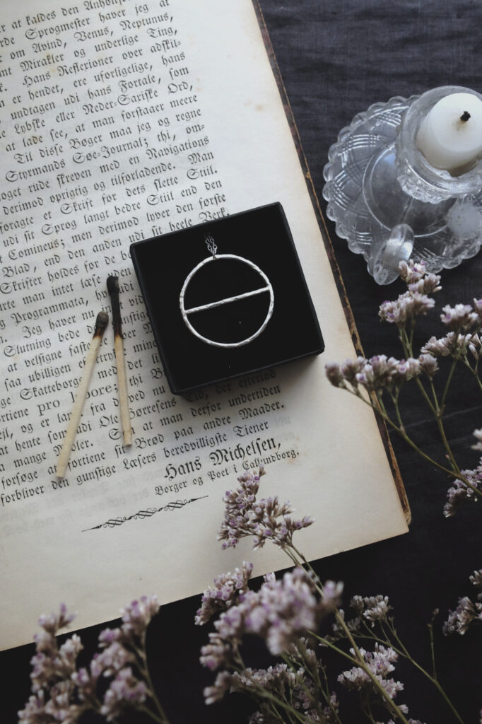 silver pendant of the alchemical symbol Salt on an antique book, with a candle