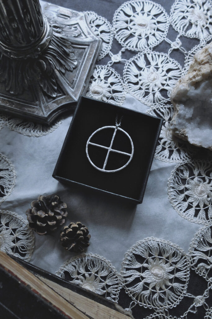 silver pendant of the alchemical symbol Earth on a doily