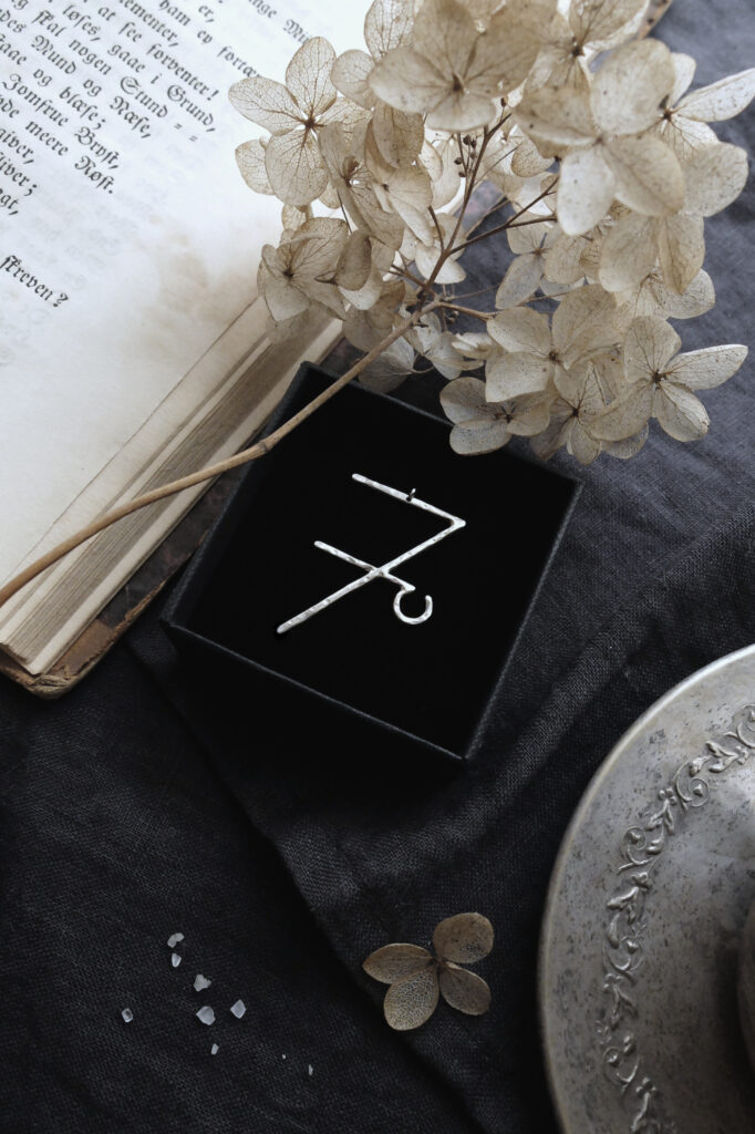 silver pendant of the alchemical symbol Vitriol with an antique book and dried flowers