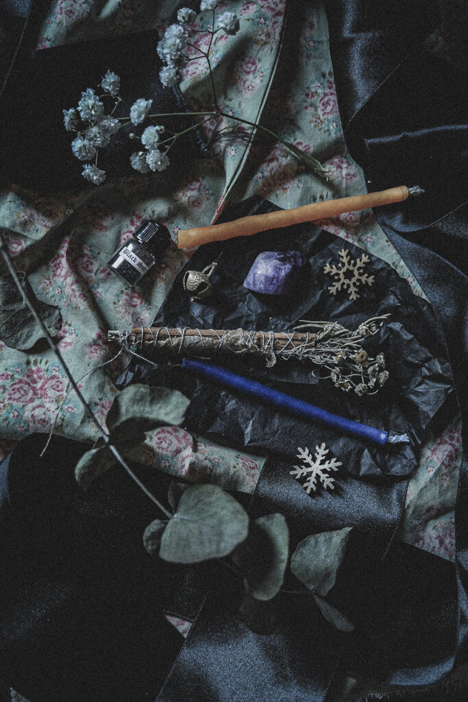 dark still life with black salt, bell, amethyst, mini candles, dried flowers and wooden snowflakes