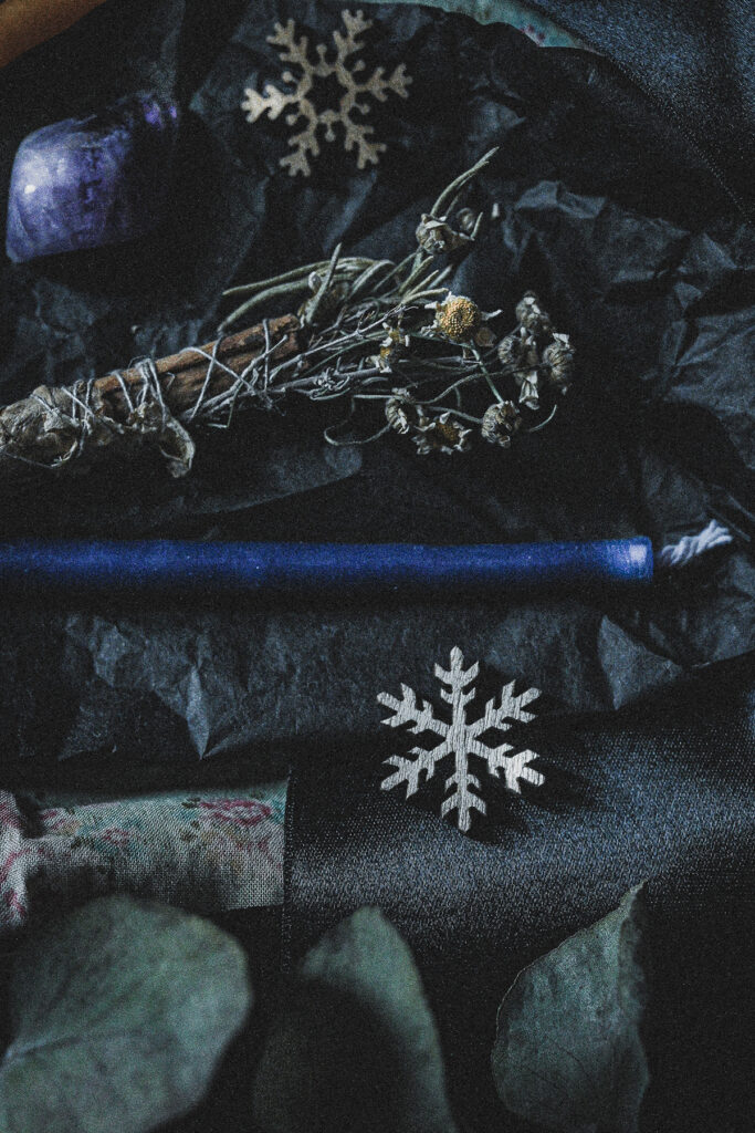 dark still life with amethyst, a smoke wand, a mini candle and wood snowflakes
